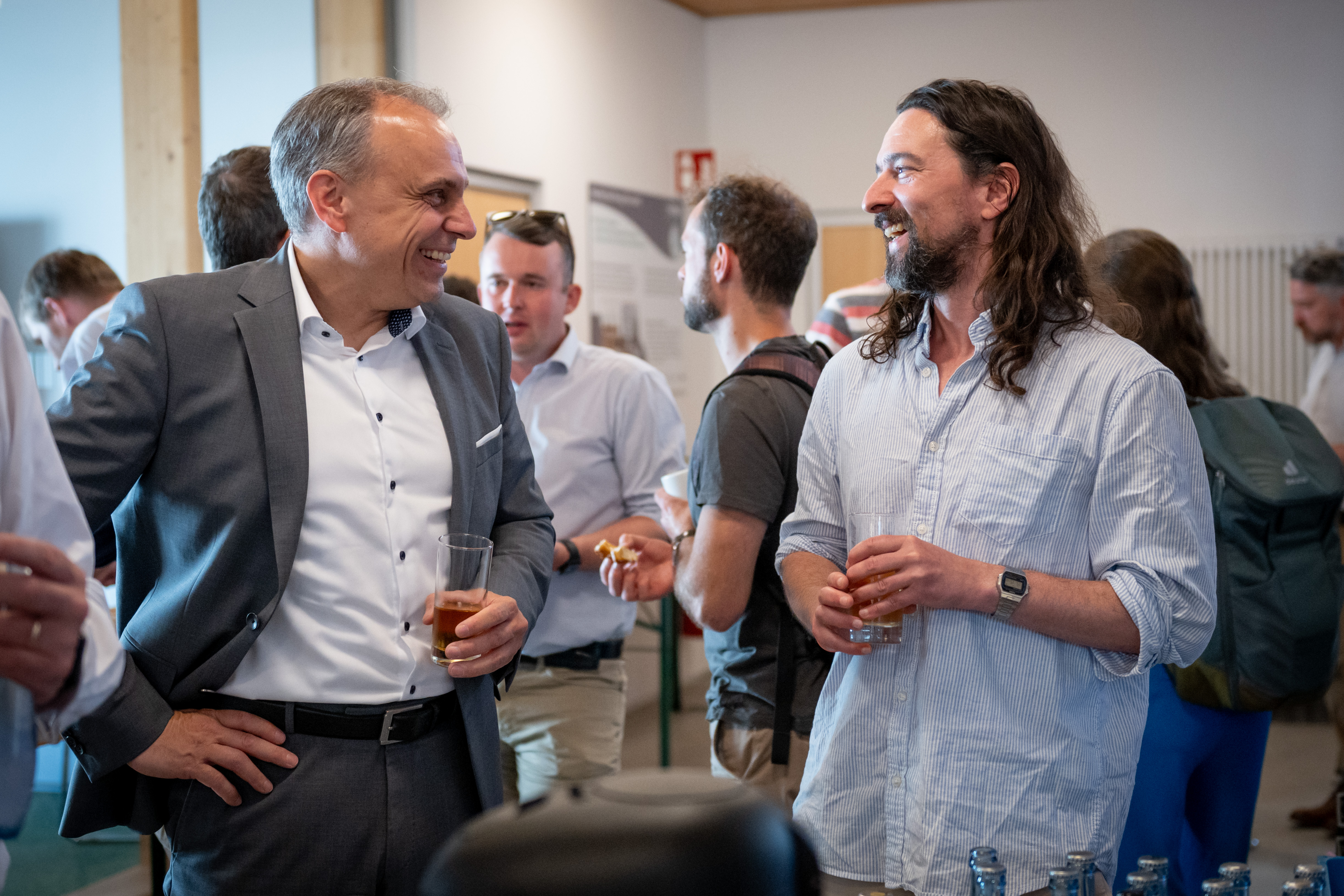 Zwei Männer im Gespräch bei einer Networking-Veranstaltung mit Getränken in den Händen.