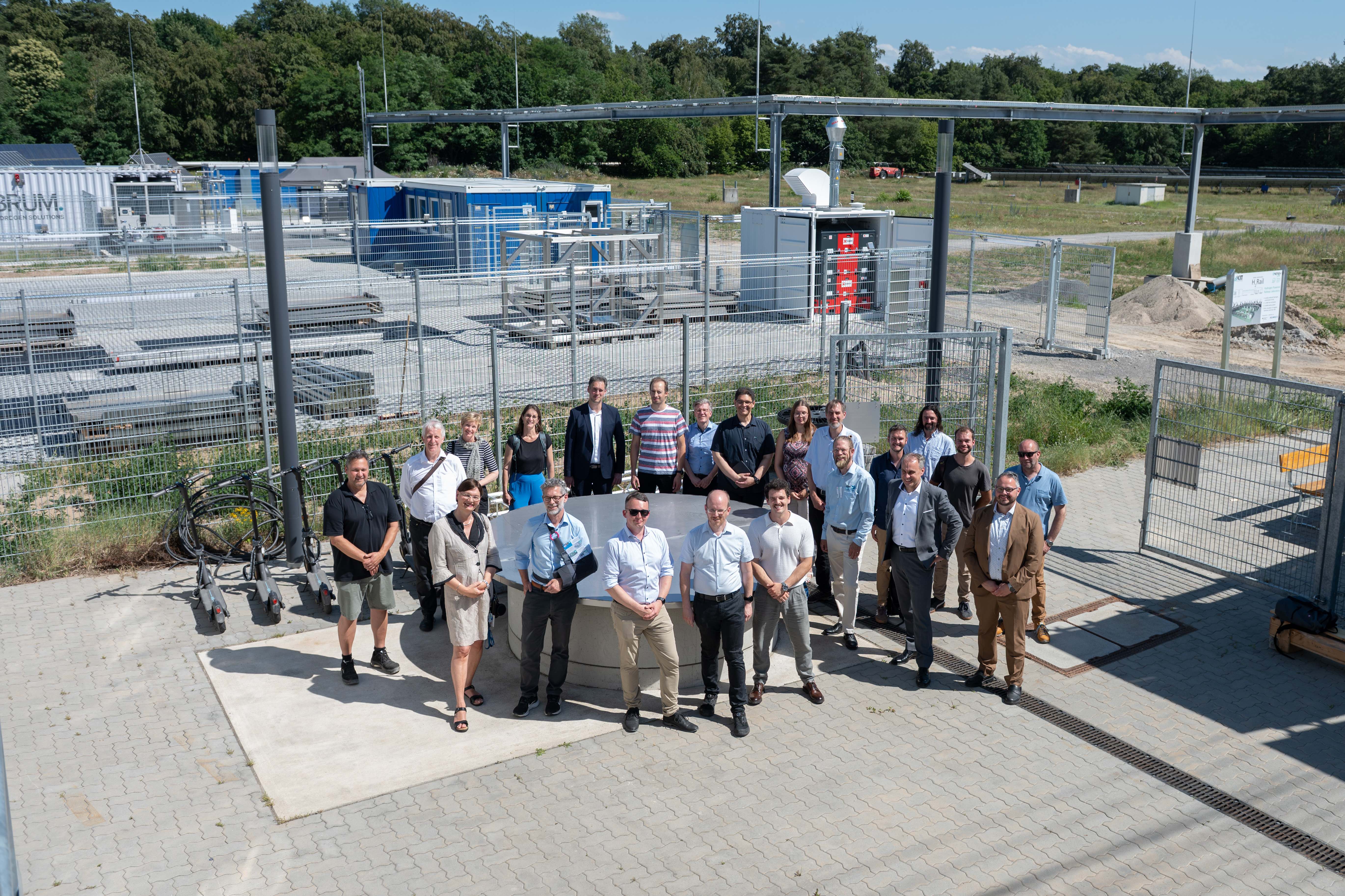 Gruppenfoto einer Arbeitsgruppe vor einer technischen Industrieanlage im Freien.